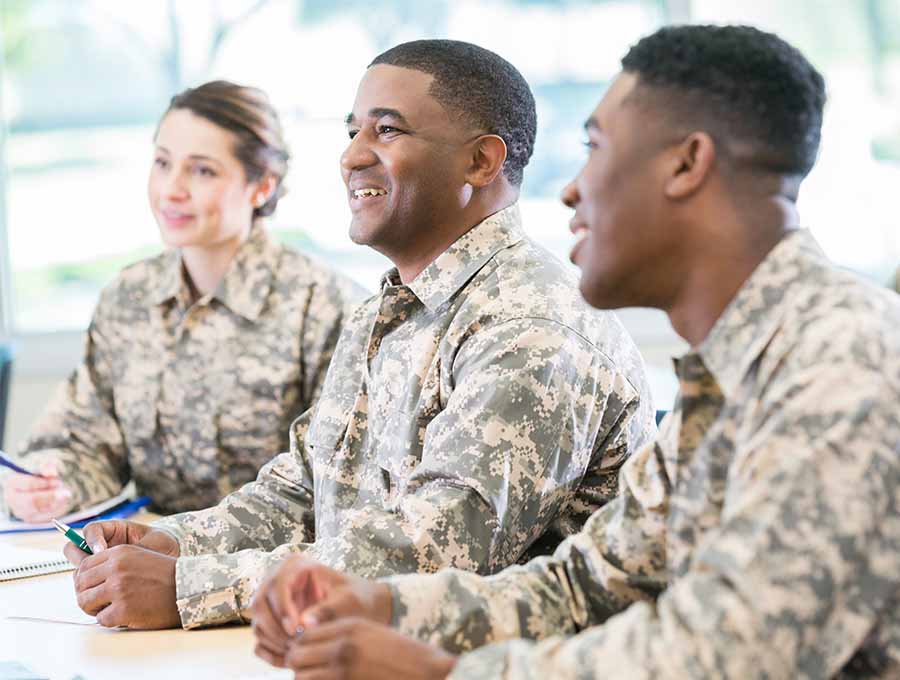 Three military students smiling at a table in a classroom.