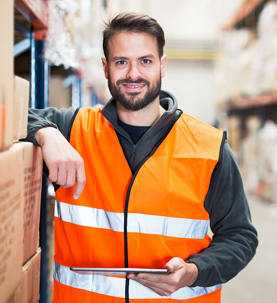 Guy wearing a safety vest holding a clip board standing in a warehouse.